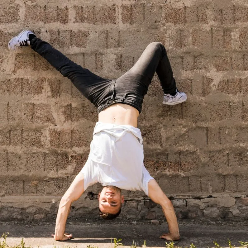 Person doing a handstand against a brick wall, with legs spread wide and feet touching the wall.